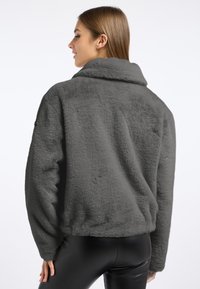 Szara kurtka z sztucznego futra z kołnierzem, luźny krój i ribbany dół. Posiada teksturowany materiał oraz obniżone ramiona.