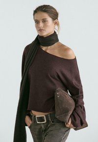 Maglione bordeaux a maglia con design scollato, abbinato a una sciarpa marrone scuro e una borsa clutch in camoscio marrone. Jeans di denim completano il look.