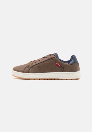 Zapatilla atlética de ante marrón con acentos de cuero azul marino, acabado texturizado, puntera redonda, entresuela blanca y suela de goma. Detalle del logo rojo en el costado.