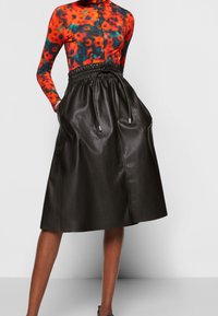 Svart läderkjol med dragsko i midjan och sidfickor. Kombinerad med en långärmad topp med flerfärgat blommönster.