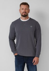 Sweatshirt en coton gris à manches longues, col rond côtelé et écusson logo sur la poitrine. Associé à un jean en denim bleu.