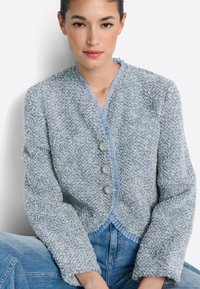 Texturált világoskék dzseki bordás gallérral, három gombos záródással és hosszú ujjal, puha kötött anyagból készült.