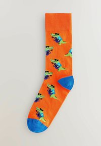 Orange sokker med grønne alligatorer iført blå outfits, solbriller og lilla accenter. Blå tåsektion, ribbet tekstur foroven.