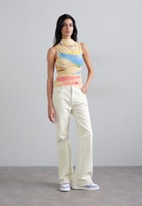 Ärmlös topp i batikmönster i gula, blå och rosa nyanser, tillsammans med krämfärgade vida byxor. Outfiten har en figurnära design och lättviktsmaterial.