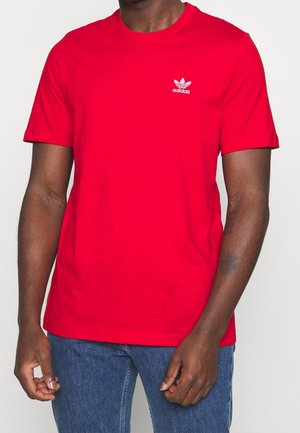 Czerwona bawełniana koszulka z okrągłym dekoltem i krótkimi rękawami. Posiada małe białe logo Adidas na lewej piersi. Gładka tekstura.