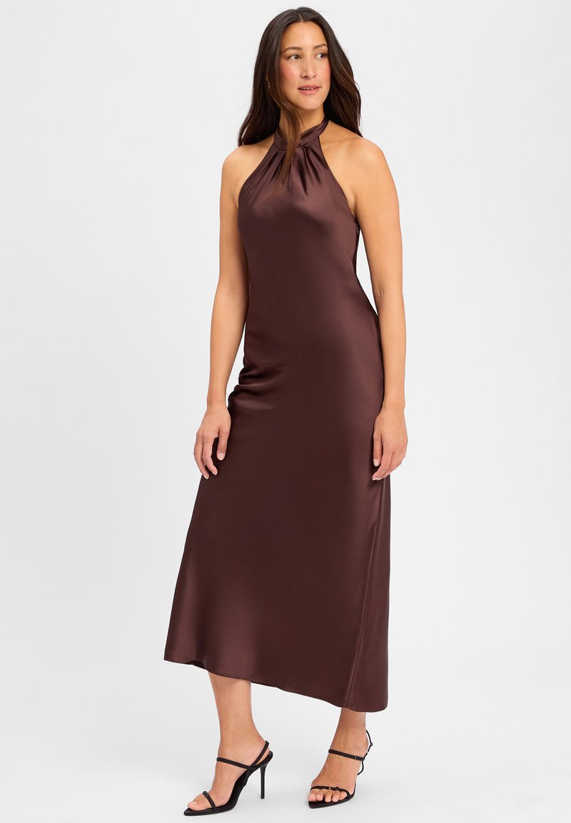 Robe halter en satin marron, corsage ajusté, jupe fluide, texture lisse, longueur cheville, associée à des sandales à talons noirs à brides.