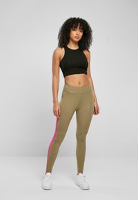 Svart cropped topp og olivengrønne leggings med en rosa stripe. Glatt, elastisk stoff; tettsittende design; hvite sneakers. Enkel, moderne stil.