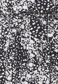 Šaty s černobílým vzorem vyrobené z texturované látky, s mašlí v pase a nabranými detaily, vytvářejícími splývavou siluetu.