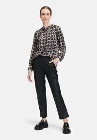 Black and beige patterned long-sleeve top with a round neckline, paired with black, tapered cargo pants and chunky black shoes.