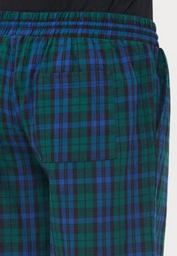 Pantalon à carreaux avec un motif vert, bleu et noir. Fabriqué en tissu léger, avec une taille élastique et des poches latérales.