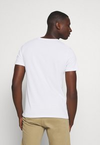 Camiseta blanca de manga corta con cuello redondo, fabricada en algodón. Diseño simple sin logotipos ni patrones visibles, adecuada para el uso diario.