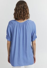 Niebieska, luźno dopasowana bluzka z krótkimi, marszczonymi rękawami. Posiada okrągły dekolt i miękką, gładką fakturę. Prosty design, brak wzorów.