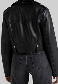 Musta lyhyt nahkatakki, jossa on jäsennelty muotoilu, leveä kaulus ja hopeiset painikkeet. Sileä tekstuuri, jossa näkyvät ompelusaumat.