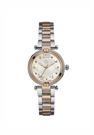 Reloj redondo con una pulsera de metal bicolor en tonos plateados y dorados. Presenta un dial de nácar, números romanos y acentos texturizados.