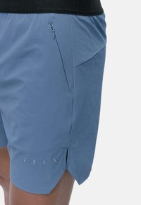 Ljusblå shorts i mjukt tyg, med en sidoficka med dragkedja och splittat fåll. Diskreta logodetaljer nära fållen.