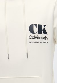 Λευκό φούτερ με κουκούλα με μαύρο λογότυπο Calvin Klein, μεγάλα γράμματα "CK" και κείμενο "Established 1968" στο στήθος, με κορδόνια με μεταλλικά άκρα.