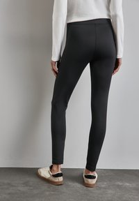 Leggings noirs avec une texture extensible et lisse, un design ajusté et une taille haute, associés à des baskets beiges et noires.