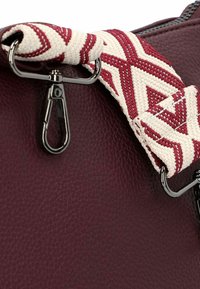 Bordeauxfarbene Ledertasche mit strukturiertem Oberflächen, ausgestattet mit einem gemusterten geflochtenen Tragegurt in Weiß und Rot, gesichert mit silberfarbener Hardware.