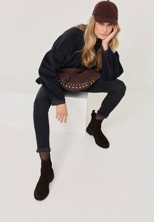 Bruine suède enkelbooties met elastische zijpanelen, een platte zool, gecombineerd met zwarte jeans en een zwarte oversized sweater.