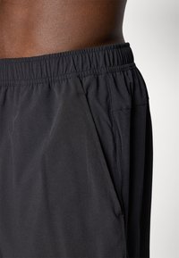 Black athletic shorts featuring an elastic waistband, side pockets, and a smooth, lightweight fabric with minimal sheen.