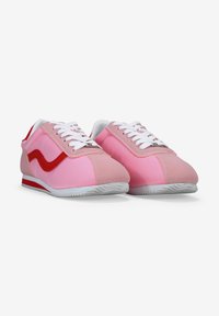 Zapatillas rosas de tela con acentos rojos en contraste, cordones blancos y una suela texturizada, que presentan una punta redondeada y un perfil bajo.