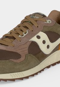 Baskets en marron, olive et beige avec tissu texturé et panneaux en daim, semelles beiges et lacets marron, montrant les détails sur le côté et le dessus.