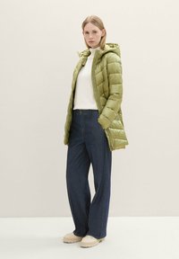 Giacca a vento verde chiaro con cappuccio, design trapuntato, abbinata a un dolcevita bianco e jeans a gamba larga blu scuro. Scarpe color crema.