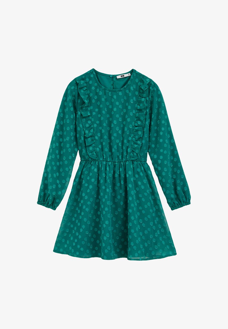 Zelena haljina s dugim rukavima, okruglim izrezom, naboranim prednjim dijelom i strukom zdjelice. Ima točkasti uzorak i suknju koja se širi.