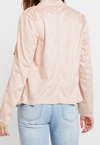 Ljust rosa fuskmockajacka med långa ärmar, skräddarsydd passform och en ren bakseam. Matchad med ljusblå denimjeans.