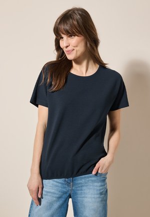 Top de manga corta azul marino con cuello redondo y tejido texturizado, que presenta un corte relajado y un dobladillo recto. Llevado con jeans de color azul claro.