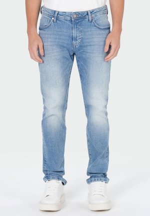 Light blue slim-fit jeans worn with white sneakers and a white t-shirt on a standing person against a plain background.