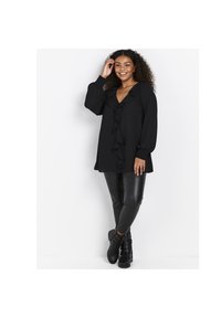 Svart tunika med volang framtill, långa ärmar och v-formad halsringning, ihop med åtsittande svarta byxor och ankelkängor. Slät kvalitet, avslappnad design.