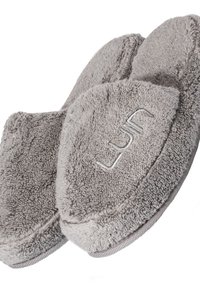 Grå plyschtofflor med mjuk, fluffig textur, rund form och subtila sömdetaljer som pryder varumärkesnamnet.