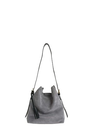 Sac seau en suède gris avec une finition texturée, une bandoulière noire réglable et un accent de pampille décorative. Design à ouverture supérieure.