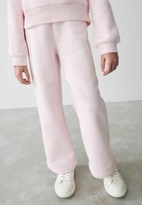 Rosa sweatshirt och matchande sweatpants, båda i mjukt tyg, har ribbade manschetter och en avslappnad passform, som kombineras med vita sneakers.