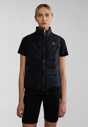 Navy puffer vest with high collar, front zipper, and horizontal quilting. Worn over a black shirt and paired with black biking shorts.