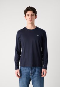 Navy long-sleeve T-shirt made of cotton with a round neckline and white "HUGO" logo on the chest. Model wearing blue jeans.