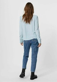 Hellblaues Langarmbluse mit glatter Textur, kombiniert mit hoch taillierten blauen Jeans und schwarzen klobigen Stiefeln.