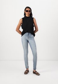 Haut sans manches noir avec des plis verticaux, jeans skinny bleu clair avec des détails déchirés, et ballerines à imprimé animal avec des brides noires.