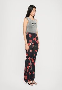 Gråstripet ermeløs topp med teksten "Moschino Jeans"; høyt liv svarte bukser med stort rødt blomster mønster; svarte hæl sandaler.