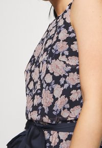 Námořnické květinové šaty s růžovými růžemi a zelenými listy, s přiléhavým korzetem a zavazovací páskou v odpovídajícím materiálu.