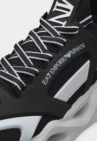 Ασπρόμαυρο αθλητικό παπούτσι EA7 Emporio Armani με χοντρές ριγέ κορδόνια και λεπτομέρειες από δίχτυ στο επάνω μέρος.
