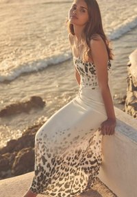 Abito maxi senza spalline in tessuto leggero, con una base bianca e stampa leopardata nera. Texture liscia e silhouette fluida.
