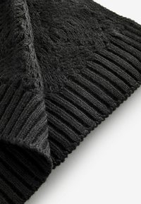 Textile noir tricoté avec un motif texturé, présentant une bordure côtelée. Le matériau semble doux et confortable, adapté aux temps froids.