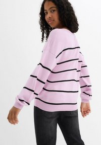 Maglione rosa chiaro con strisce orizzontali nere, vestibilità rilassata, maniche lunghe e polsini a costine, abbinato a jeans scuri.