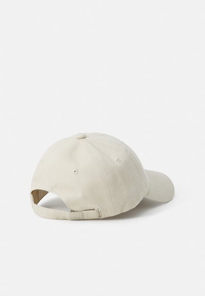 Beige bomullsbaseballcaps med buet skjerm, justerbar stropp og seks ventilasjonsøyne. Glatt tekstur med quilted finish.