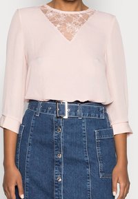 Helles rosa Bluse mit Spitzen-V-Ausschnitt, kombiniert mit einem hochtaillierten blauen Jeansrock mit Knopfleiste vorne und einem beltmten Taillendesign.