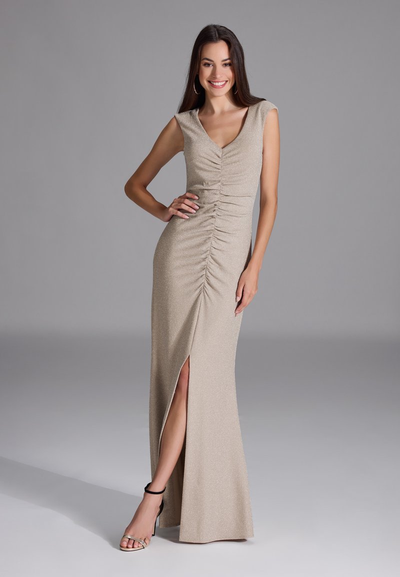 Béezhiv gown, joka on vartalon myötäinen, mihin kuuluu hihattomat hihat, rypytetty yläosa, reiden ylle ulottuva halkio ja kimaltava pinta, joka on yhdistetty mustiin nilkkareleet-kenkiin.