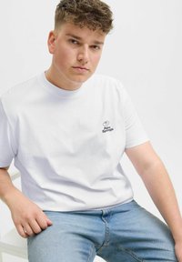 Hvid bomulds t-shirt med korte ærmer, der har et lille blåt "Palm Springs" logo på brystet. Kombineret med lyseblå jeans.