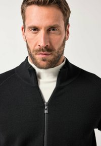 Maglione nero con zip, dotato di un alto colletto, realizzato in tessuto morbido. Presenta una zip metallica e motivi a costine sul colletto e sulle maniche.